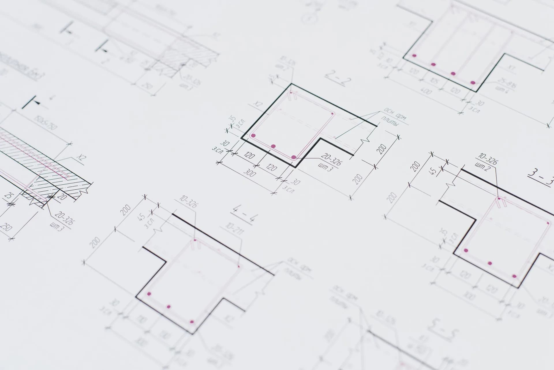 Close-up of large-format technical drawings on a desk, marked up by hand in red.